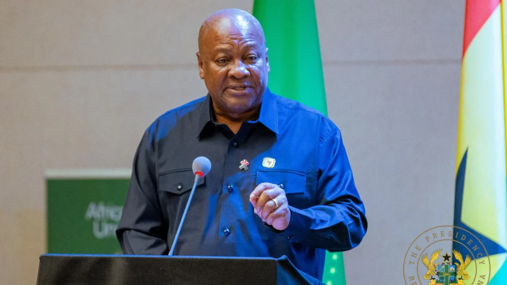 John Mahama speaking at an official podium with the Ghanaian flag and presidential seal in the background, addressing national economic policies and the minimum capital requirement for foreign investors.